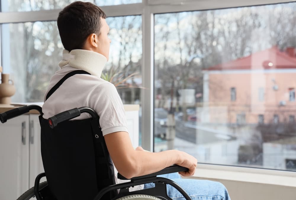 Young man in wheelchair, injured from accident at home, looks concerned and in discomfort.