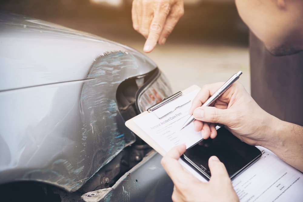Inspecting and documenting car damage for insurance claim, with clipboard and smartphone in use.